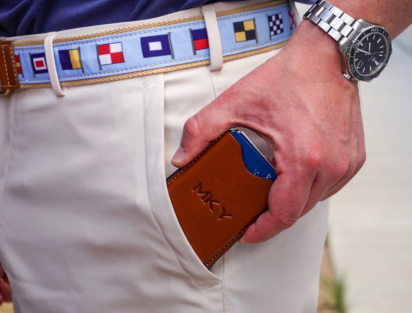 A close-up of a hand pulling a sleek leather money clip from the pocket of white trousers.