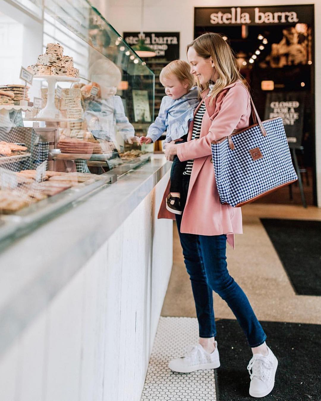 Charming moment of mother and child picking treats at a bakery with a blue checkered personalized handbag