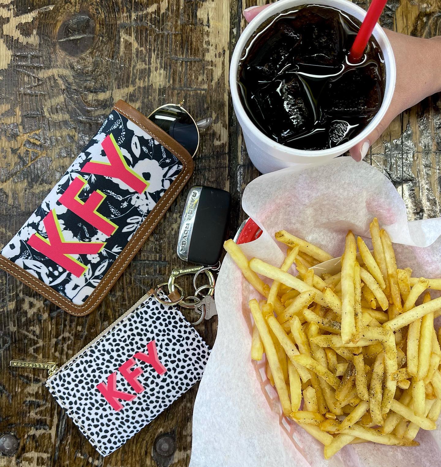 Black floral design zip wallet keychain on table with fries and drink