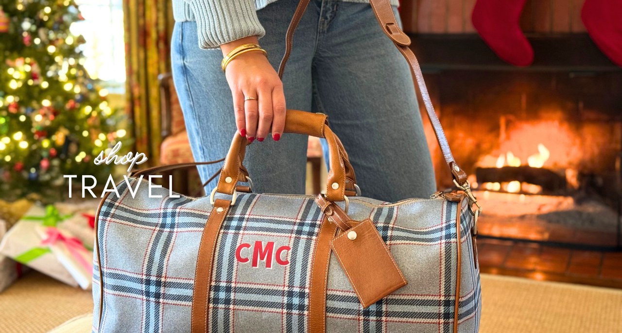Personalized plaid travel duffle bag with red monogram and leather luggage tag by Christmas fireplace